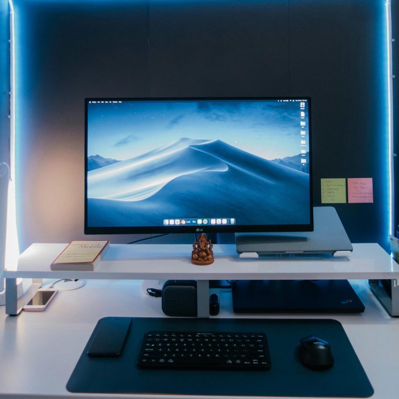Modern desk setup with illuminated monitor, keyboard, mouse, and neat arrangement under soft neon lights.